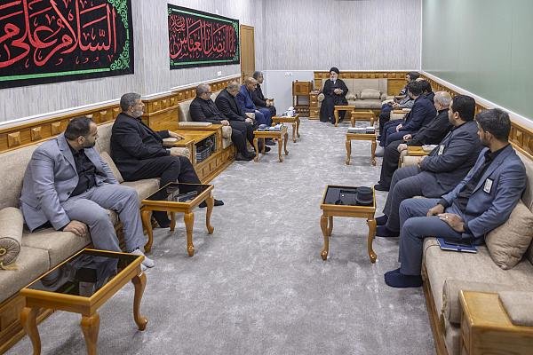 رجل دين معمم يجتمع بوفد من الرجال في قاعة استقبال رسمية.