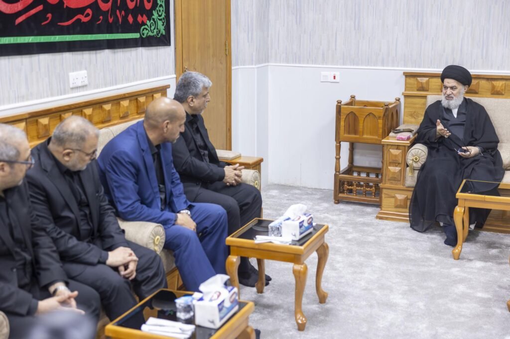 رجل دين معمم يتحدث إلى جانب من الوفد الزائر في قاعة استقبال.