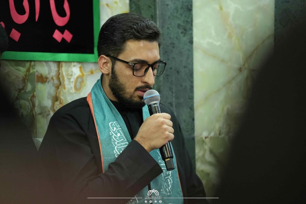شاب يرتدي نظارة ووشاحاً أخضر يتحدث في الميكروفون.