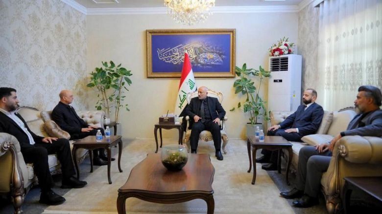مسؤول يستقبل وفداً رسمياً في مكتبه بحضور عدد من الشخصيات وتحت العلم العراقي.