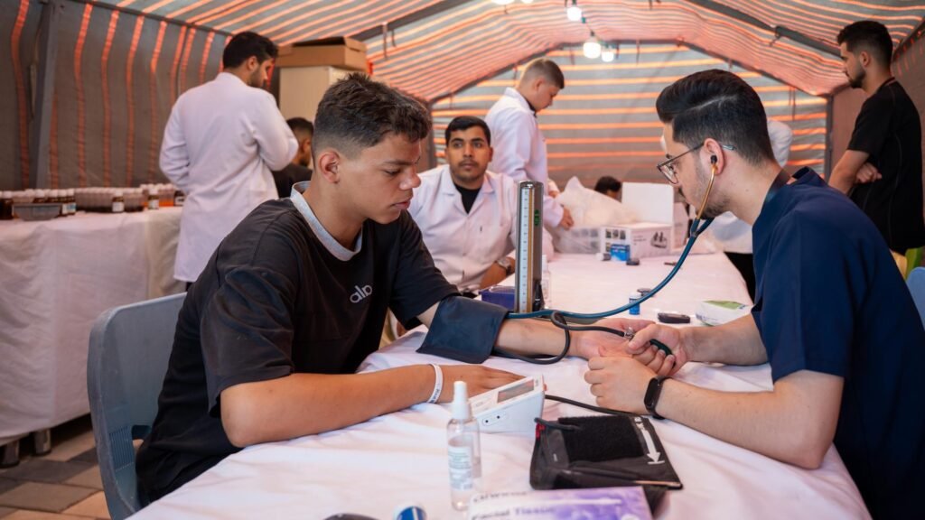 طبيب يستخدم السماعة الطبية ليفحص نبض وضغط شاب زائر داخل خيمة المفرزة الصحّة.