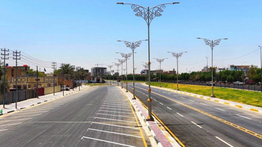شارع حديث متعدد المسارات مزود بإنارة زخرفية وتخطيط مروري ومساحات خضراء.