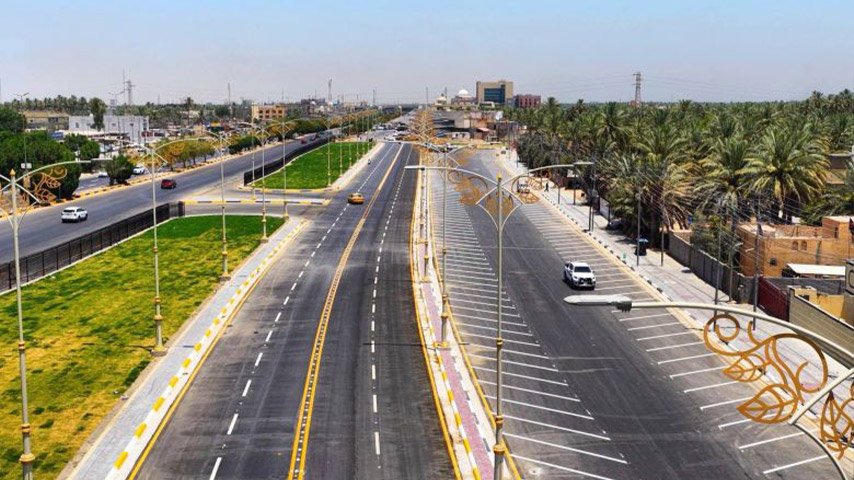 شارع حديث متعدد المسارات تحيط به مساحات خضراء ومواقف جانبية وأعمدة إنارة زخرفية.