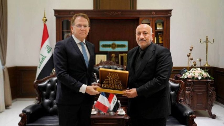 مسؤول عراقي ومسؤول أجنبي يتبادلان درعاً تذكارياً يحمل اسم كربلاء خلال لقاء رسمي.