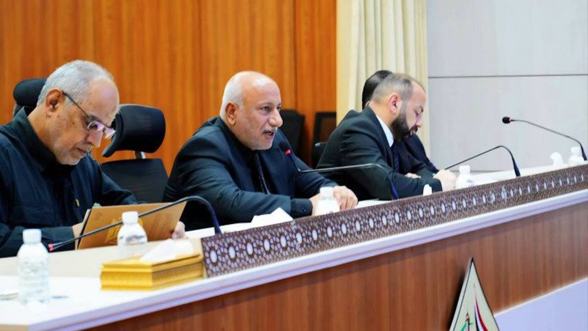 مسؤولون يشاركون في اجتماع رسمي داخل قاعة مؤتمرات، ويتحدث أحدهم عبر الميكروفون بينما يدون الآخرون الملاحظات.