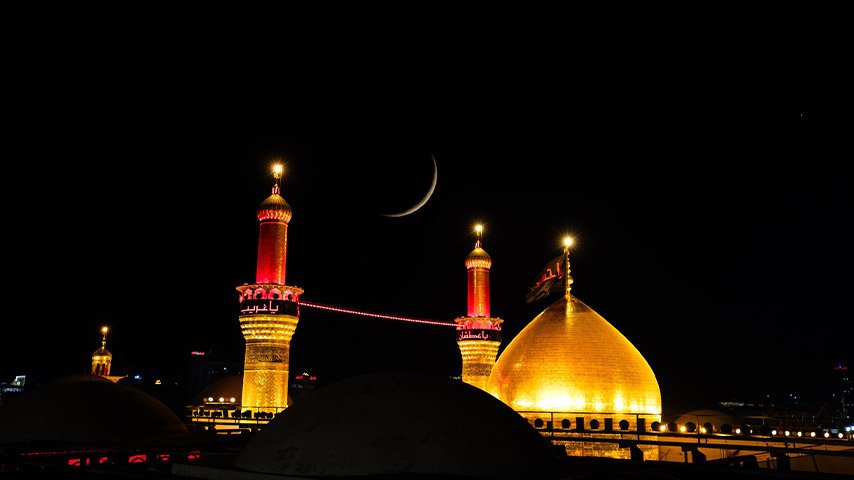قبة ذهبية ومئذنتان مضاءتان ليلاً في كربلاء.