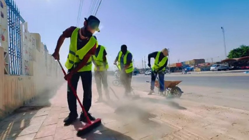 عمال نظافة ينظفون رصيفاً بمحاذاة أحد الشوارع.