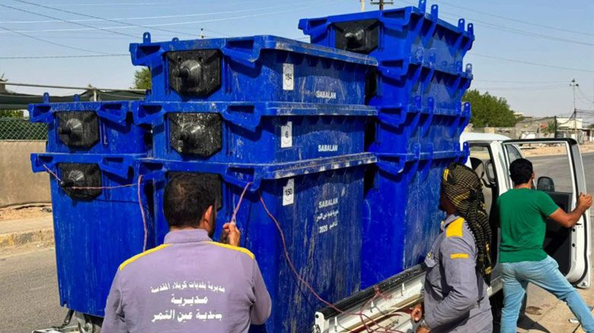 عمال بلديات ينزلون حاويات نفايات زرقاء من شاحنة نقل.