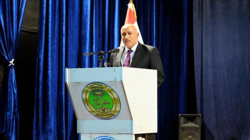 محافظ كربلاء يلقي كلمة من على منصة خطابة أمام ستارة زرقاء.