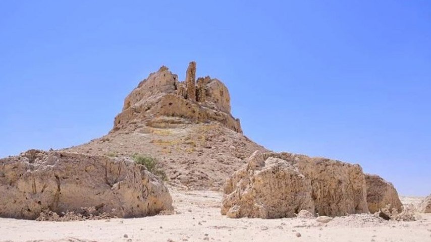 تل صحراوي مرتفع تعلوه أطلال حجرية متهدمة تحيط به صخور كبيرة واسعة