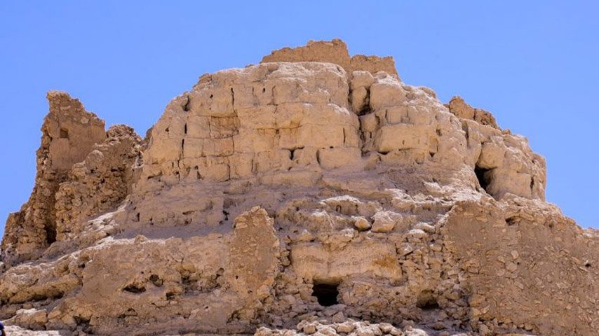 بقايا جدران وأسوار طينية متهدمة لقصر أثري فوق مرتفع صخري