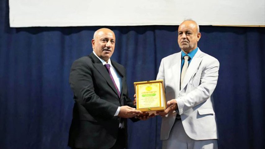 محافظ كربلاء يسلّم درعاً تكريمياً لشخص آخر خلال احتفالية.