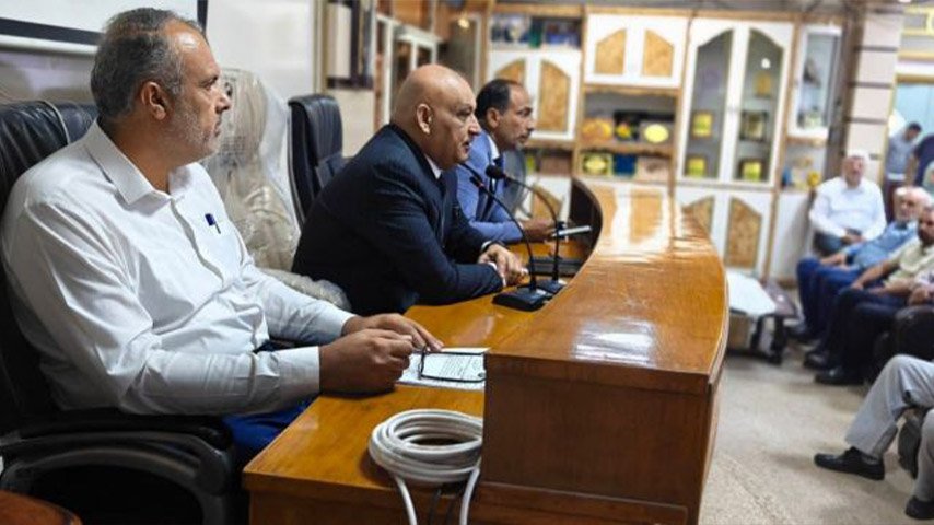 مسؤولون يجلسون خلف منصة خشبية يتحدثون أمام الحضور في القاعة