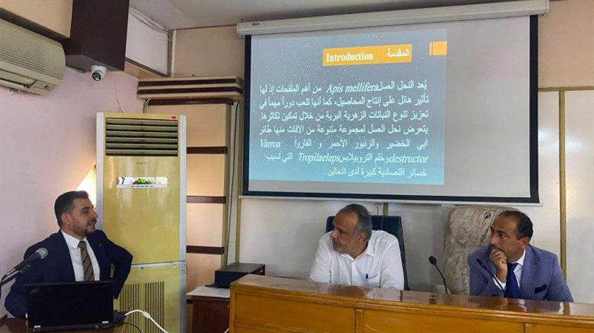 محاضر يقدم عرضًا توضيحيًا على شاشة العرض بجانب اثنين من المسؤولين داخل القاعة