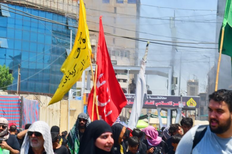 مشاة يرفعون رايات دينية خلال مسيرهم باتجاه كربلاء وسط أجواء الزيارة الأربعينية.
