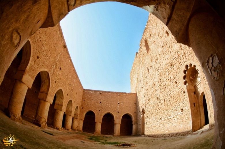 فناء داخلي واسع لحصن الأخيضر محاط بأقواس حجرية وجدران عالية تحت السماء.