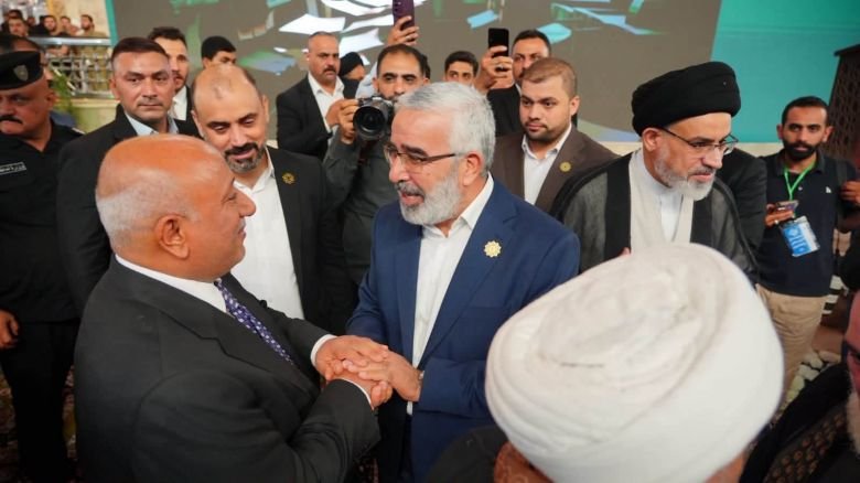 رجلان يتصافحان بحرارة وسط جمع من الحضور ورجال الدين والمصورين.