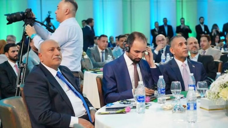 محافظ كربلاء يجلس في مقدمة القاعة بجانب مسؤولين آخرين خلال فعاليات مؤتمر رسمي.