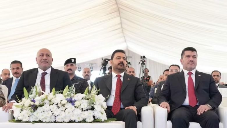 مسؤولون ببدلات رسمية وربطات عنق حمراء يجلسون على مقاعد بيضاء وأمامهم تنسيقية من الزهور البيضاء داخل خيمة احتفالات